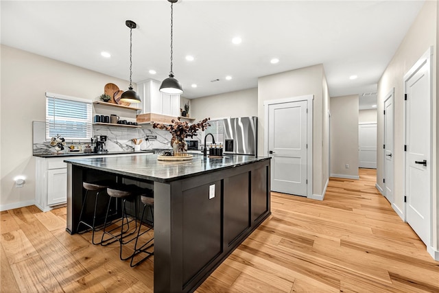 kitchen with pendant lighting, a breakfast bar area, dark stone countertops, a kitchen island with sink, and light hardwood / wood-style flooring