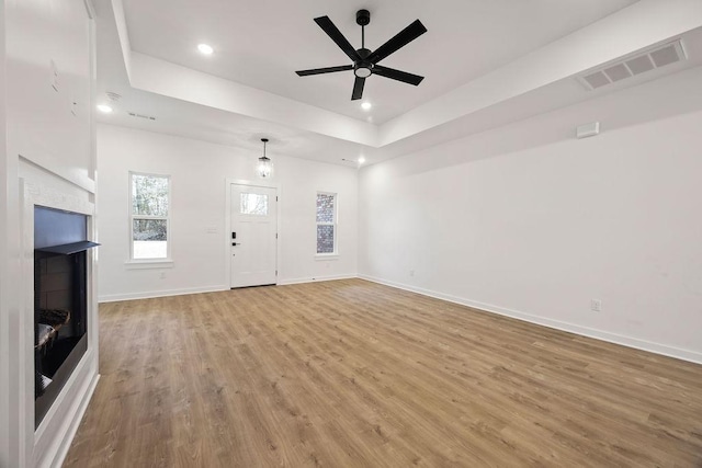 unfurnished living room featuring a fireplace, visible vents, baseboards, a tray ceiling, and light wood finished floors