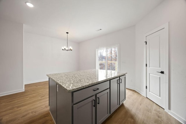 kitchen with gray cabinets, a kitchen island, light wood-style flooring, and light stone countertops