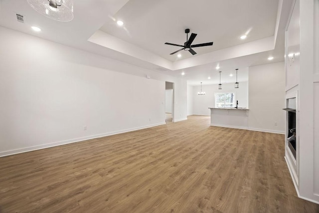 unfurnished living room with ceiling fan, recessed lighting, visible vents, light wood-style floors, and a tray ceiling