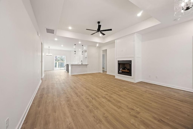 unfurnished living room with visible vents, a raised ceiling, light wood-style floors, a fireplace, and ceiling fan with notable chandelier