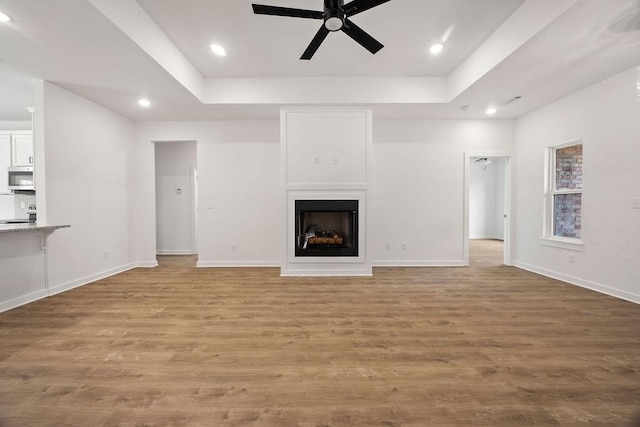 unfurnished living room with baseboards, a fireplace, a tray ceiling, and wood finished floors