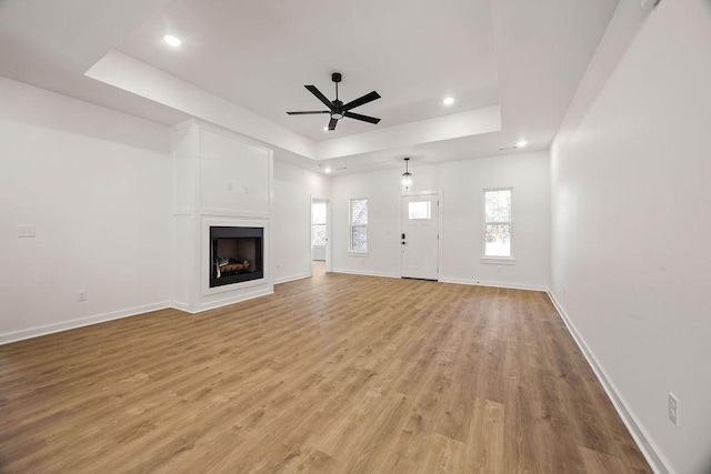 unfurnished living room featuring a raised ceiling, baseboards, a fireplace, and light wood finished floors