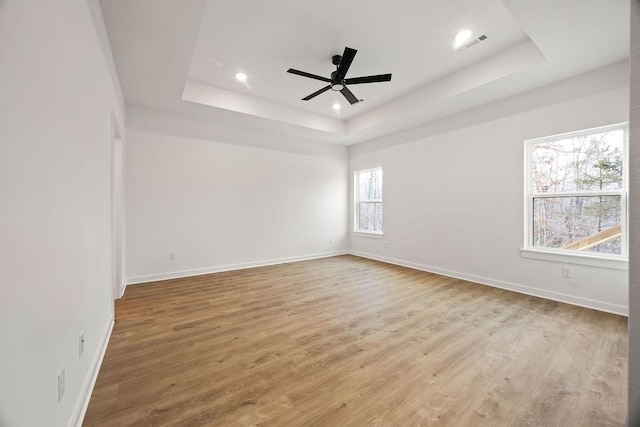 empty room featuring light wood finished floors, baseboards, and a raised ceiling