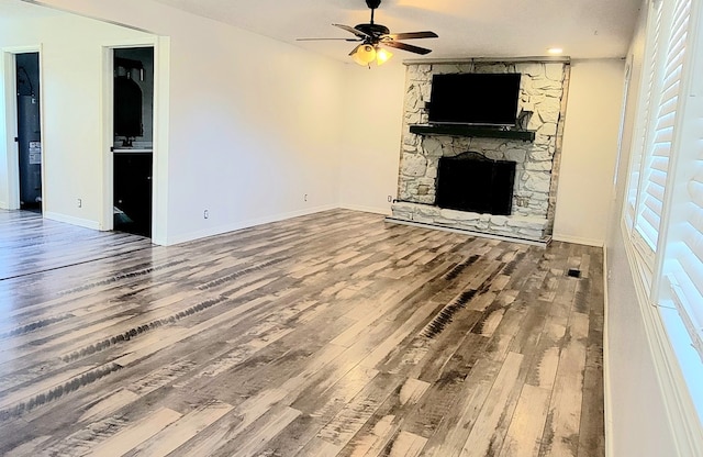 unfurnished living room featuring a stone fireplace, ceiling fan, wood-type flooring, and a textured ceiling