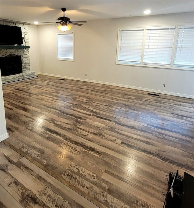 unfurnished living room with dark hardwood / wood-style floors, ceiling fan, a fireplace, and a wealth of natural light