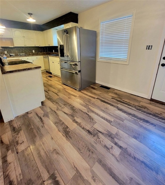 kitchen with white cabinets, light wood-type flooring, appliances with stainless steel finishes, and tasteful backsplash