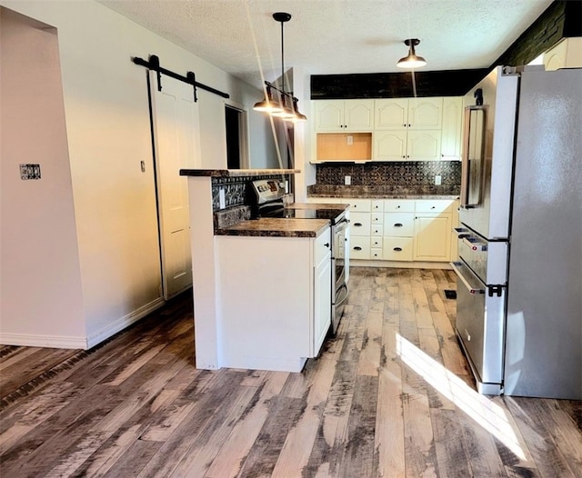 kitchen featuring a textured ceiling, stainless steel appliances, a barn door, decorative light fixtures, and dark hardwood / wood-style floors