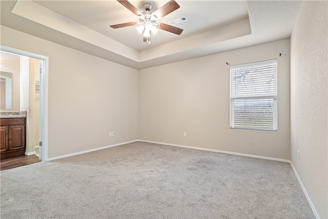 empty room with carpet, a raised ceiling, and ceiling fan