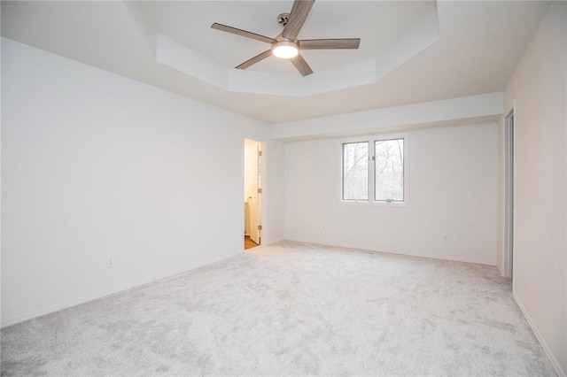 unfurnished room featuring ceiling fan, light colored carpet, and a tray ceiling