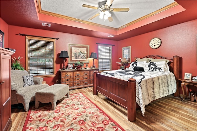 bedroom featuring a raised ceiling, ceiling fan, light hardwood / wood-style flooring, and ornamental molding