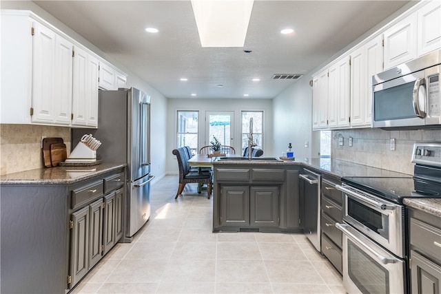 kitchen featuring stainless steel appliances, light tile patterned floors, kitchen peninsula, decorative backsplash, and white cabinets