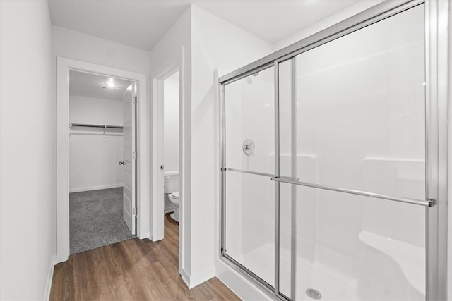 bathroom with toilet, a shower with shower door, and hardwood / wood-style flooring