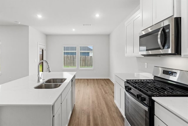 kitchen with stainless steel appliances, sink, a center island with sink, light hardwood / wood-style flooring, and white cabinetry