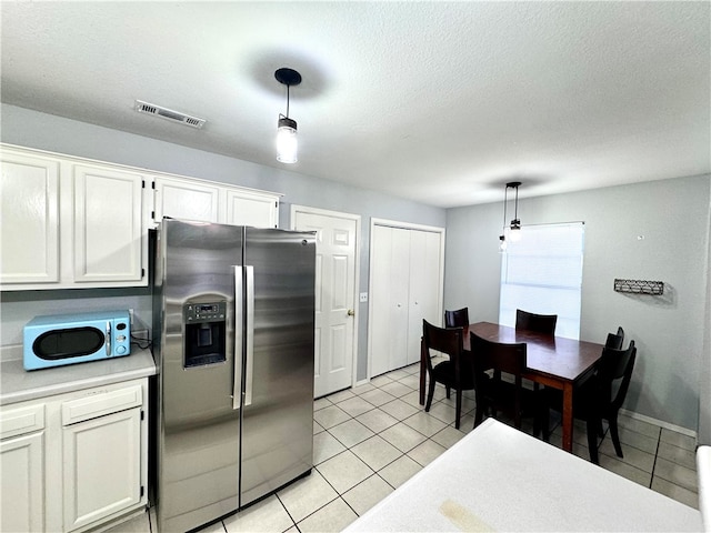 kitchen with light tile patterned floors, white cabinets, pendant lighting, and stainless steel refrigerator with ice dispenser