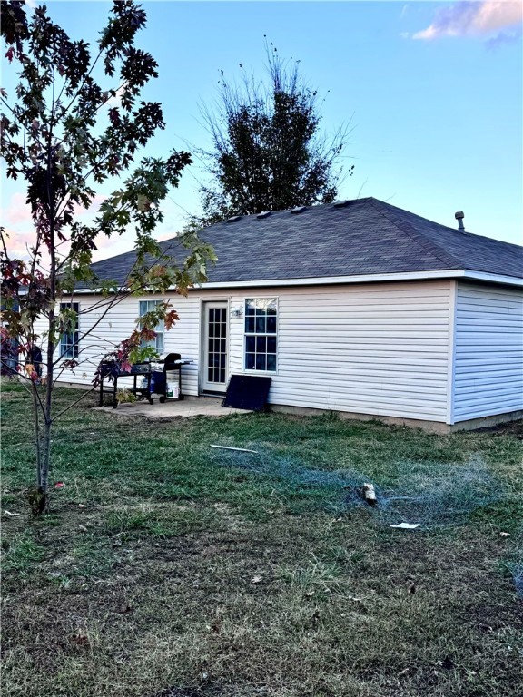 back house at dusk featuring a yard and a patio