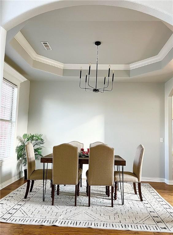 dining space featuring a raised ceiling, a chandelier, crown molding, and light hardwood / wood-style floors