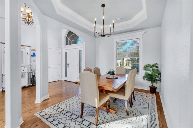 dining space featuring a raised ceiling, ornamental molding, a notable chandelier, and light wood-type flooring