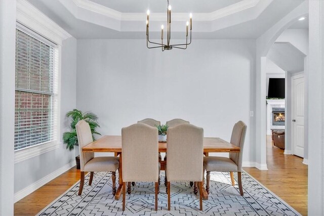 dining space featuring light wood-type flooring, a raised ceiling, ornamental molding, and a notable chandelier