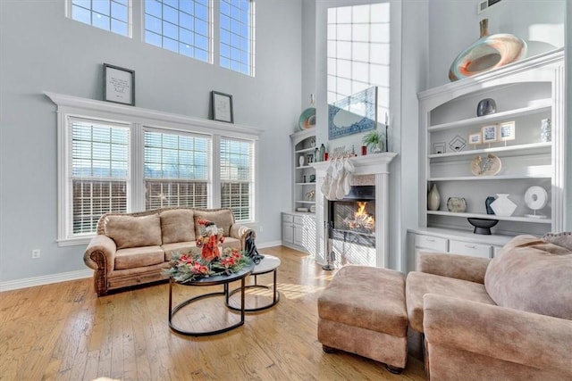 sitting room with a towering ceiling, light hardwood / wood-style flooring, built in features, and a premium fireplace