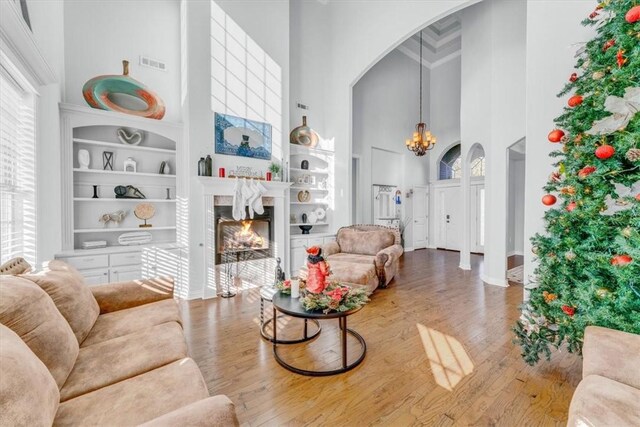 living room featuring hardwood / wood-style floors, a towering ceiling, an inviting chandelier, and built in shelves