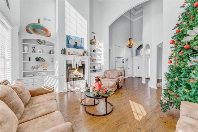 living room with hardwood / wood-style floors, built in features, a fireplace, a high ceiling, and an inviting chandelier