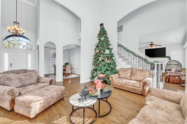 living room with ceiling fan with notable chandelier, a towering ceiling, and hardwood / wood-style flooring