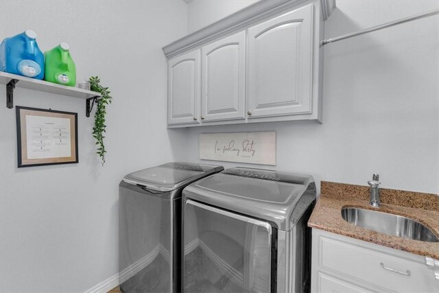 clothes washing area with separate washer and dryer, sink, and cabinets