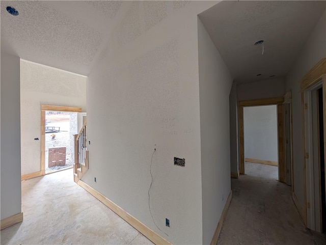 hallway featuring lofted ceiling, a textured wall, stairway, a textured ceiling, and baseboards