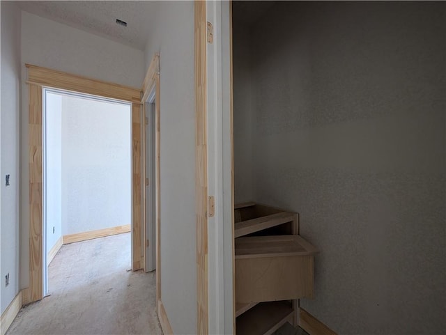 hallway featuring baseboards and unfinished concrete flooring