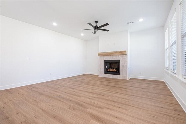 unfurnished living room featuring a tile fireplace, light wood-type flooring, and ceiling fan