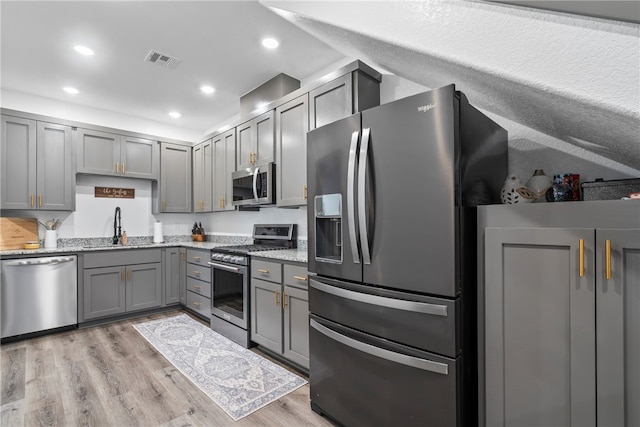 kitchen with stainless steel appliances, gray cabinetry, and light hardwood / wood-style floors