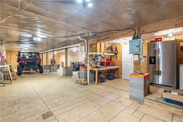 basement with stainless steel fridge with ice dispenser, a workshop area, and electric panel