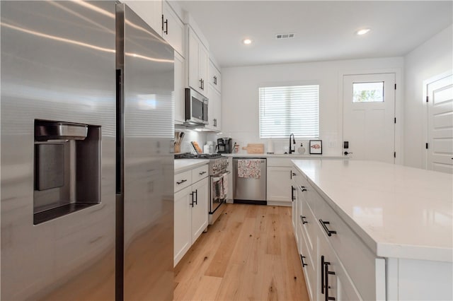 kitchen with white cabinets, light wood-type flooring, stainless steel appliances, and sink