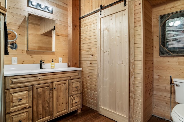 bathroom featuring wood walls, vanity, wood finished floors, and toilet