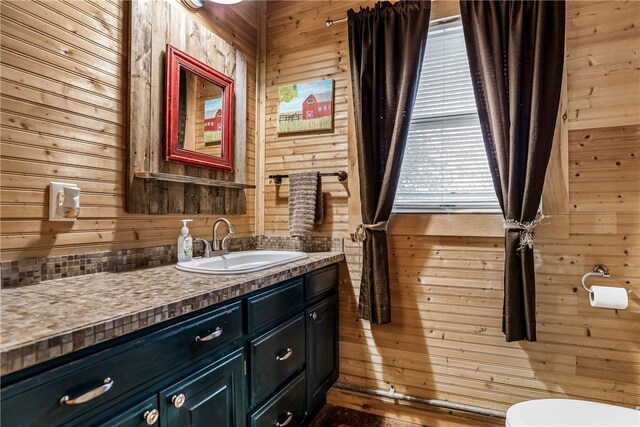 bathroom featuring toilet, vanity, and wooden walls