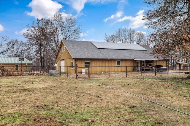 exterior space featuring fence, a lawn, a detached garage, roof with shingles, and solar panels