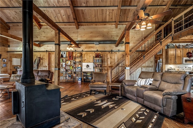 living room with beam ceiling, a wood stove, wood walls, and ceiling fan