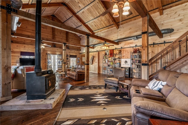 living area featuring wood walls, a wood stove, ceiling fan, and a barn door