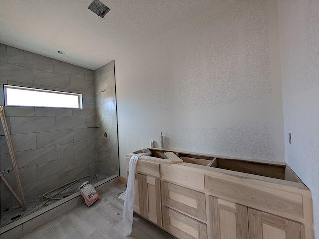 full bath featuring tiled shower and a textured wall