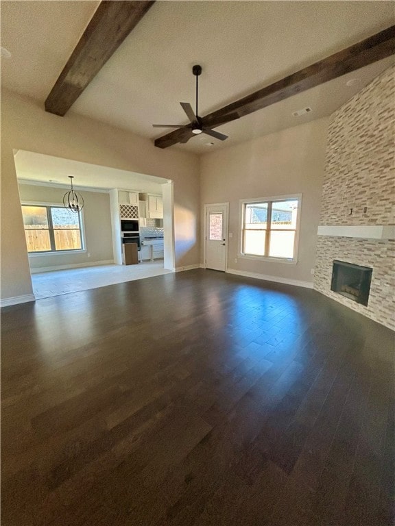 unfurnished living room featuring ceiling fan with notable chandelier, beam ceiling, dark hardwood / wood-style flooring, and a fireplace