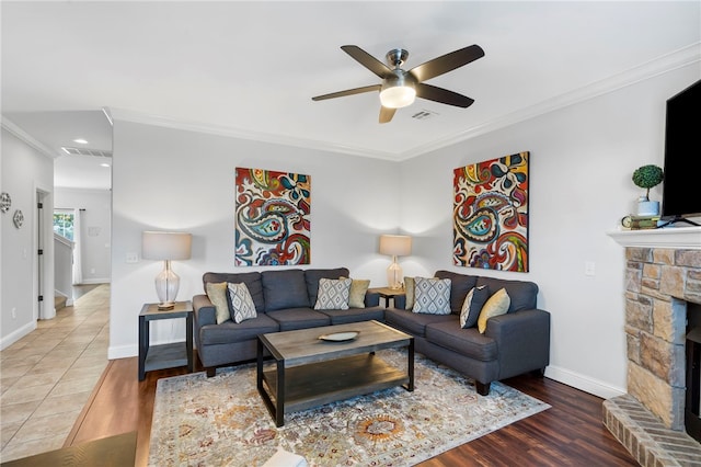 living room featuring hardwood / wood-style floors, a stone fireplace, ceiling fan, and crown molding