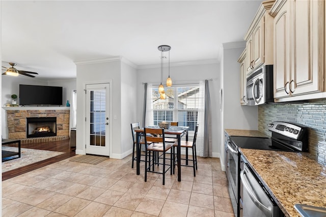 kitchen featuring ceiling fan, light stone counters, decorative backsplash, appliances with stainless steel finishes, and ornamental molding