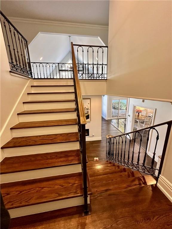 staircase with wood-type flooring, crown molding, and a high ceiling