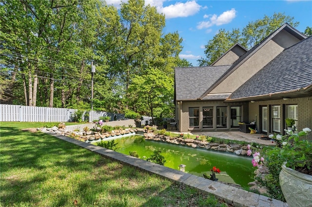 view of yard with a patio, fence, and a garden pond