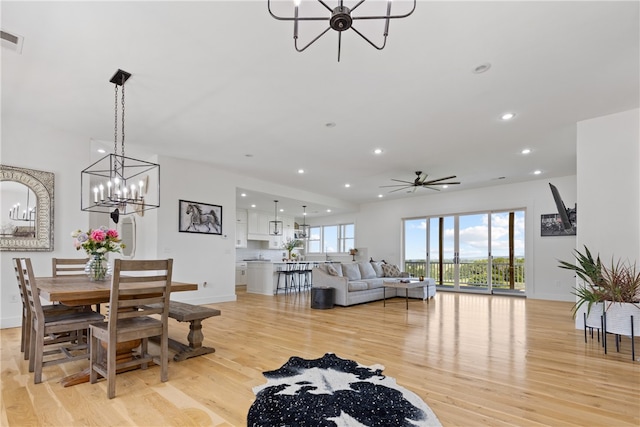 dining area with ceiling fan with notable chandelier and light wood-type flooring