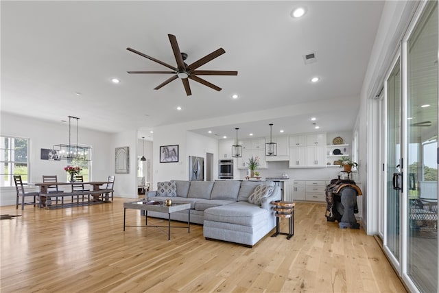 living room featuring ceiling fan with notable chandelier and light hardwood / wood-style floors