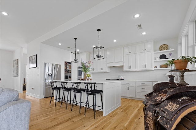 kitchen with stainless steel appliances, decorative light fixtures, white cabinetry, light hardwood / wood-style flooring, and a kitchen island