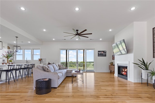 living room featuring light hardwood / wood-style flooring, ceiling fan with notable chandelier, and sink