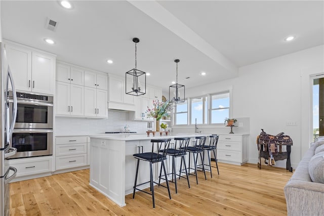 kitchen featuring white cabinets, a kitchen island, a kitchen bar, and light wood-type flooring